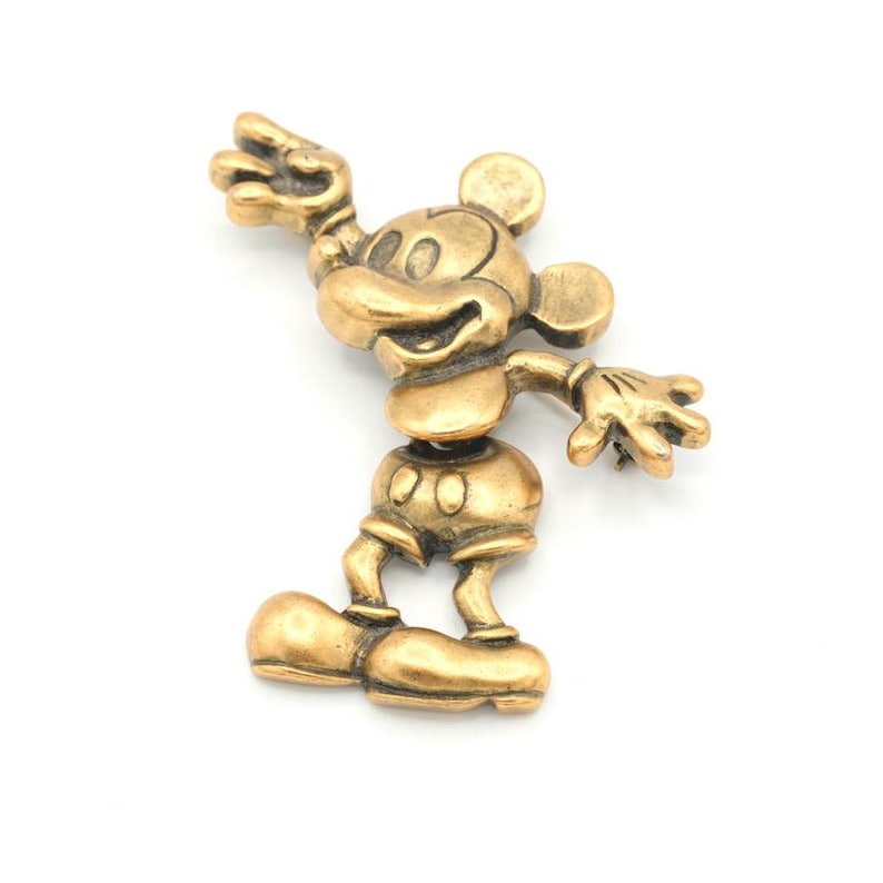 Peut inclure: Figurine dor&eacute;e de Mickey Mouse en position debout, une main lev&eacute;e et l'autre tendue. La figurine a de grandes oreilles, un short et des chaussures. Le design g&eacute;n&eacute;ral est une repr&eacute;sentation classique du personnage embl&eacute;matique.