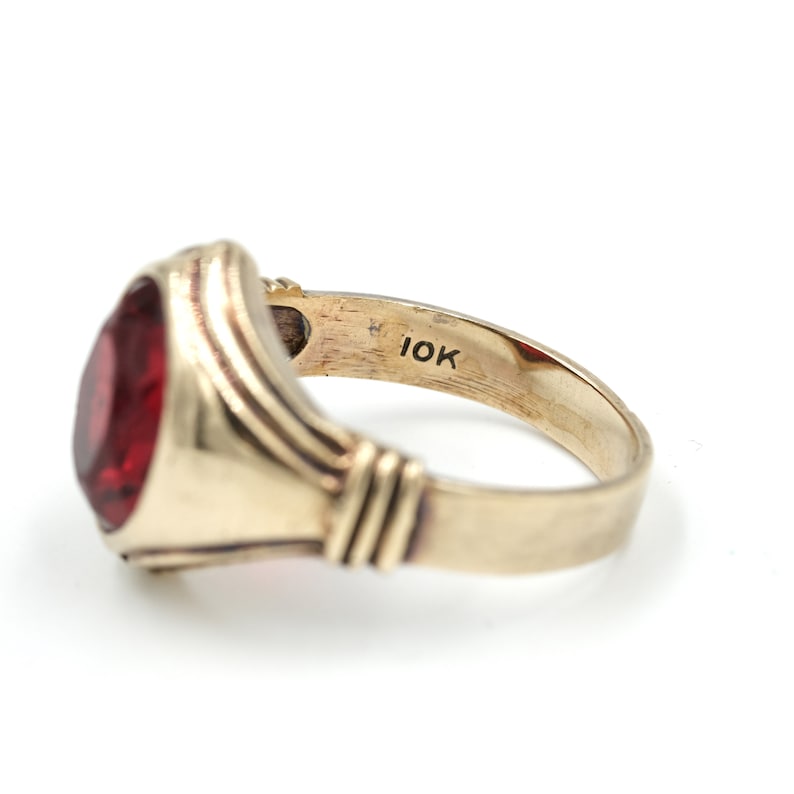May include: A gold ring with a red gemstone set in a bezel setting. The ring is marked "10K" on the inside of the band.