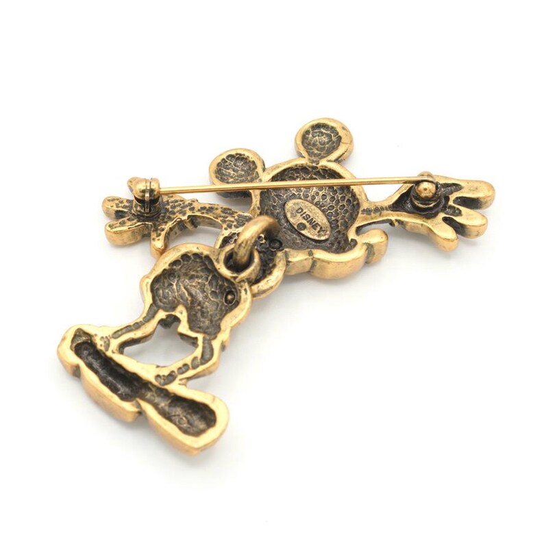Peut inclure: Broche Mickey Mouse dor&eacute;e avec fermeture &agrave; &eacute;pingle. La broche repr&eacute;sente la silhouette embl&eacute;matique de Mickey, avec sa t&ecirc;te, ses bras et ses jambes. Le dos de la broche est estampill&eacute; du mot "Disney".