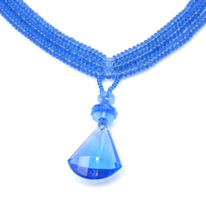 Op de afbeelding: Een blauwe kristallen ketting met een traanvormige hanger. De ketting is gemaakt van meerdere strengen kleine blauwe kralen.