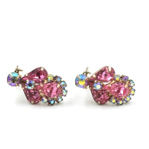 May include: A pair of pink and iridescent rhinestone earrings. The earrings are made of metal and have a cluster of pink and iridescent rhinestones in the shape of a teardrop.