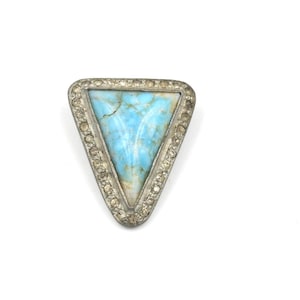 May include: A triangular brooch with a light blue stone center and a silver-colored, jewel-encrusted border. The brooch has a vintage or antique aesthetic, with a focus on the natural stone's unique patterns and color variations.
