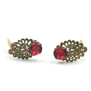 May include: A pair of gold filigree earrings with red gemstone accents.