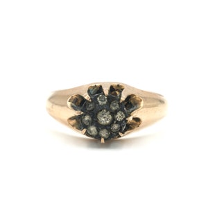 Puede incluir: Un anillo de oro con un grupo de pequeños diamantes engastados en un diseño de estrella.