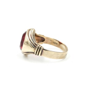 May include: A gold ring with a red gemstone set in a bezel setting. The ring is marked "10K" on the inside of the band.