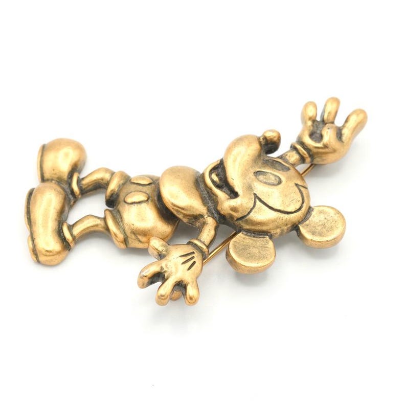 Peut inclure: Broche en m&eacute;tal dor&eacute; repr&eacute;sentant Mickey Mouse allong&eacute;, les bras et les jambes tendus. La broche est munie d'une &eacute;pingle au dos pour l'attache. Le design est de style vintage, avec un aspect l&eacute;g&egrave;rement vieilli.
