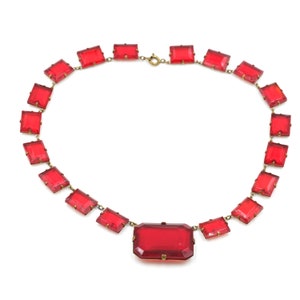 May include: A red glass necklace with a large rectangular pendant. The necklace is made of smaller rectangular glass stones connected by a gold chain.