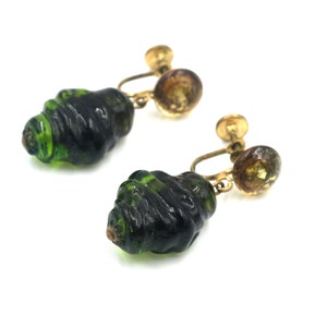 May include: A pair of vintage green glass clip-on earrings with gold tone metal accents. The earrings feature a swirl design and a round, amber-coloured glass bead.