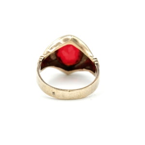 May include: A gold ring with a large, red gemstone set in a heart-shaped bezel. The ring has a simple band and is designed in a vintage style.