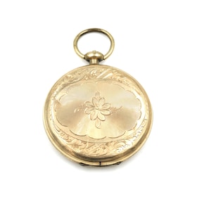 May include: A gold-colored pocket watch with an oval floral design on the front. The watch has an ornate engraved pattern around the floral design and a ring at the top for attaching a chain. The watch is set against a white background.