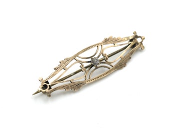 May include: A gold filigree brooch with a single diamond in the center.