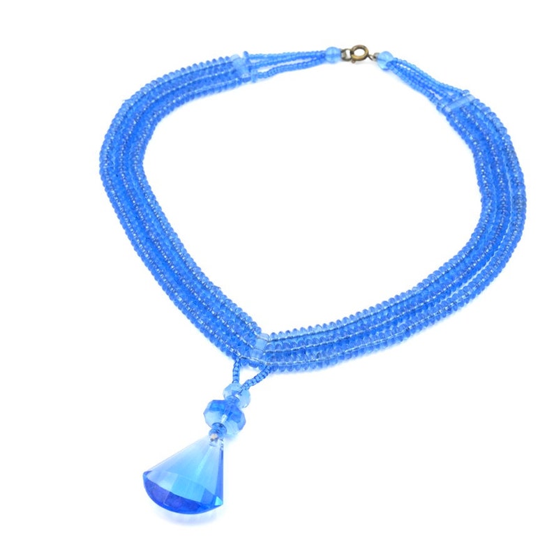 Op de afbeelding: Een blauwe kristallen ketting met een grote traanvormige hanger. De ketting is gemaakt van meerdere strengen kleine blauwe kralen.