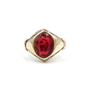 May include: A gold ring with a large, red, faceted gemstone set in a diamond-shaped bezel.