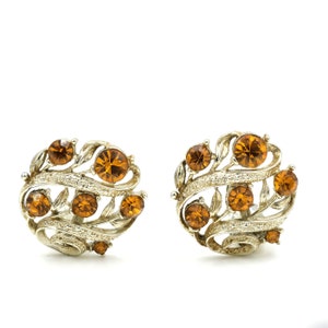 May include: A pair of gold tone clip-on earrings with a swirling leaf design and amber colored rhinestones.