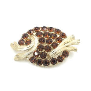 May include: A gold tone brooch with a swirl design and brown rhinestones.