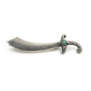 May include: A silver-toned brooch in the shape of a scimitar with a turquoise gemstone set in the handle.