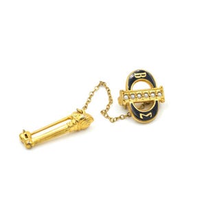May include: Gold sorority pin with a black enamel circle with the letters "BM" and a row of pearls. The pin is attached to a gold chain and a gold torch.