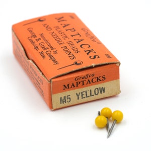 May include: A box of 100 yellow Graffco Maptacks with plastic heads and needle points. The box is orange and has the text "Graffco Maptacks Plastic Heads and Needle Points" and "M5 Yellow" printed on it.