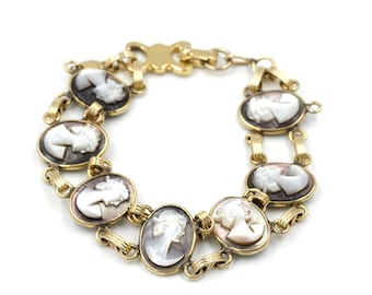 May include: A gold chain bracelet with seven oval-shaped cameo charms featuring white and brown profile portraits of women.