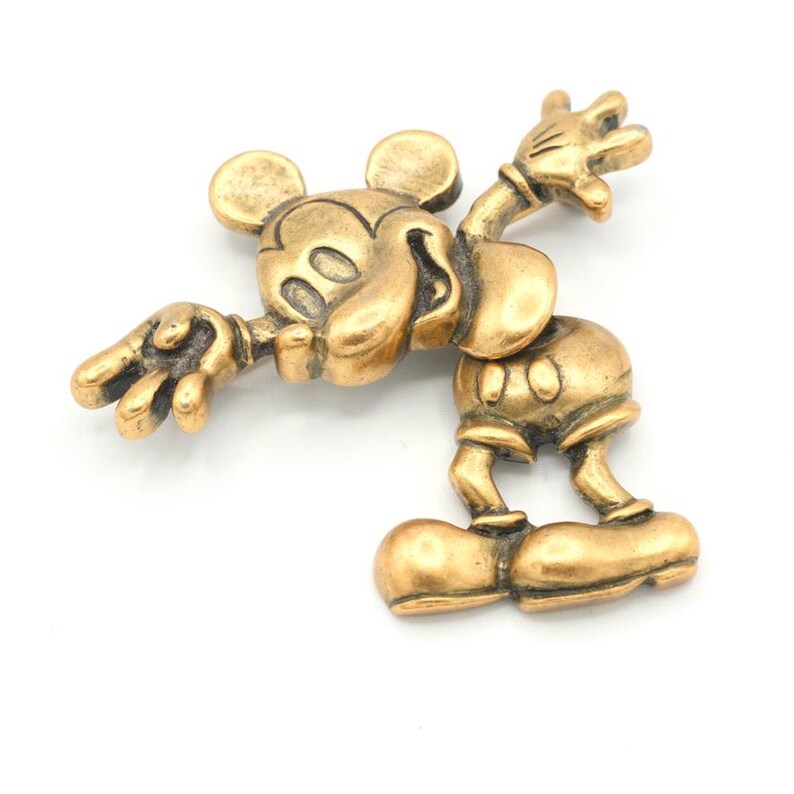 Peut inclure: Figurine dor&eacute;e de Mickey Mouse dans une pose dynamique, les bras et les jambes tendus. La figurine pr&eacute;sente les caract&eacute;ristiques distinctives de Mickey, comme ses grandes oreilles et son sourire. Fabriqu&eacute;e en m&eacute;tal, elle pr&eacute;sente des d&eacute;tails complexes.