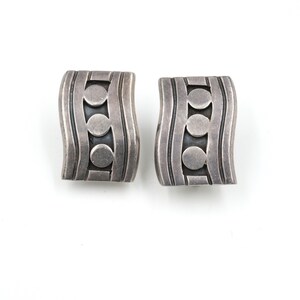 May include: A pair of silver earrings with a wavy design and three circles in the center.