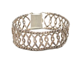 May include: A silver bracelet with a delicate, intricate design. The bracelet is made of a series of interwoven loops that create a lattice-like pattern.