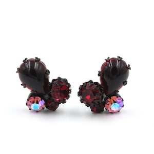 May include: A pair of dark red and black earrings with a cluster of rhinestones. The earrings feature a large teardrop-shaped stone in the center.