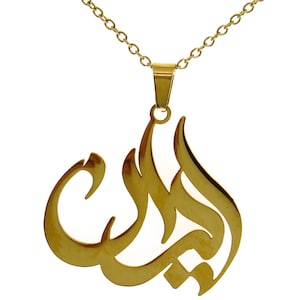 Può includere: Una collana con pendente dorato con calligrafia araba. Il pendente, a forma di fiamma o goccia stilizzata, è sospeso a una delicata catena. La collana è probabilmente realizzata in acciaio inossidabile o metallo placcato oro.