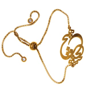 Puede incluir: Un brazalete ajustable de oro con un dije de nombre personalizado. El dije está en un estilo de escritura cursiva y presenta pequeños diamantes de imitación transparentes.