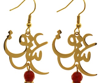 May include: Gold earrings with a red stone dangle. The earrings feature a delicate design of Arabic calligraphy.