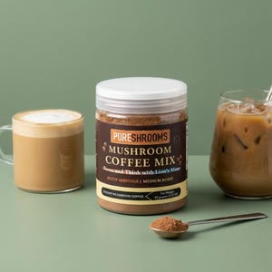May include: A jar of PURESHROOMS MUSHROOM COFFEE MIX with a white lid, a cup of coffee, and a glass of iced coffee. The jar has a brown label with text that reads "Focus and Think with Lion's Mane". A spoon of coffee mix is in front.