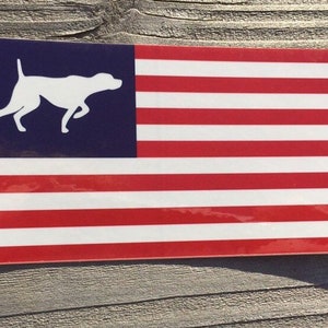 May include: A white silhouette of a dog running to the right, on a blue background, with a red, white, and blue American flag design below.