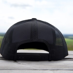 Puede incluir: Gorra de b&eacute;isbol negra con parte trasera de malla y cierre ajustable a presi&oacute;n. La gorra est&aacute; sobre una superficie de madera. El nombre de la marca "PACIFIC" es visible en la correa ajustable.