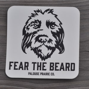 May include: White square coaster with a black and white illustration of a dog's face. The text "FEAR THE BEARD" is printed in black below the image. The text "PALOUSE PRAIRIE CO." is printed in black below the text "FEAR THE BEARD".