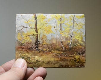 Op de afbeelding: Een schilderij van een herfstlandschap met drie bomen op de voorgrond. De bomen hebben gele bladeren en staan tegen een lichtblauwe lucht. De grond is bedekt met bruine en gele bladeren.