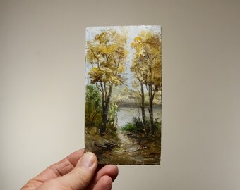 May include: A small oil painting on canvas depicting a landscape scene with two trees with yellow leaves in the foreground and a lake in the background.