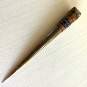 May include: A brown henna cone with a black label that says "Jagua Henna". The label has a mandala design.