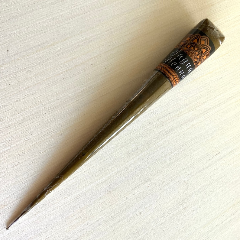 May include: A brown henna cone with a black label that says "Jagua Henna". The label has a mandala design.