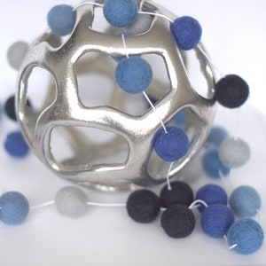May include: A silver metal sphere with a geometric design, decorated with a garland of blue and gray felt balls.