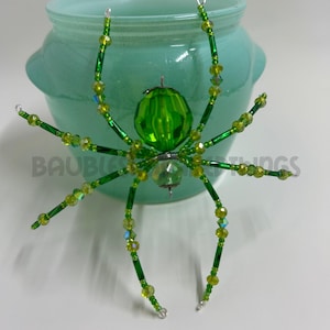 May include: A green beaded spider ornament with a crystal body and iridescent green beads. The spider is sitting on top of a light blue ceramic jar.