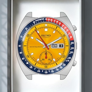 May include: A framed wall art print featuring a detailed illustration of a Seiko automatic watch with a vibrant yellow dial, a blue and red tachymeter bezel, a day-date window, and a sub-dial. The watch face displays the text Seiko Automatic.