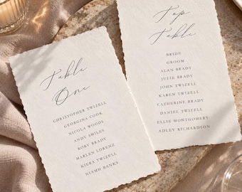 Könnte beinhalten: Zwei rechteckige, cremefarbene Papierkarten mit Büttenrand und schwarzem Textdruck. Eine Karte zeigt Table One gefolgt von einer Namensliste. Die andere Karte zeigt Top Table gefolgt von einer Namensliste, inklusive Bride und Groom.