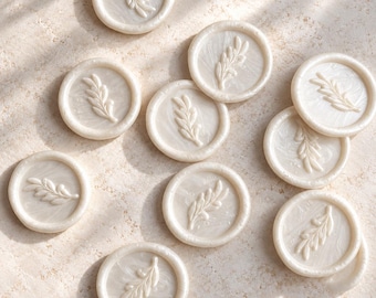 Puede incluir: Una colección de diez sellos de cera circulares en color blanco roto nacarado. Cada sello presenta un diseño en relieve de una delicada rama o ramita de hojas. Los sellos tienen una textura suave, ligeramente marmolada y un borde elevado.