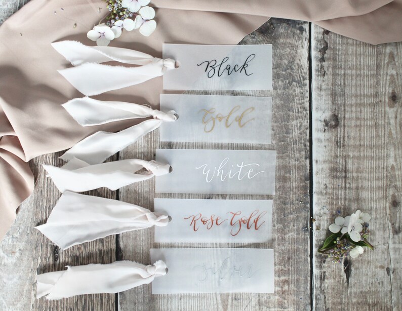 May include: Five white cards with different coloured calligraphy on each. The cards are labelled "Black", "Gold", "White", "Rose Gold", and "Silver".