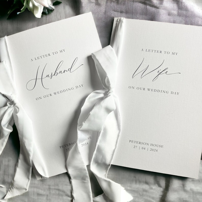May include: Two white books with white ribbon ties. The book on the left has the text "A Letter to My Husband On Our Wedding Day" and the date "27 04 2024". The book on the right has the text "A Letter to My Wife On Our Wedding Day" and the date "27 04 2024".