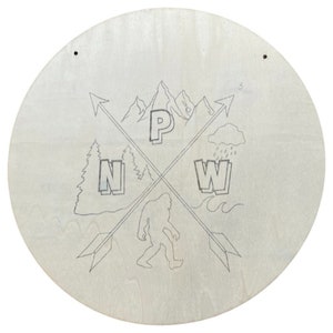 Pode incluir: Um sinal redondo de madeira com um desenho em preto e branco de uma cordilheira, um P&eacute; Grande, uma nuvem com chuva e uma onda. O sinal tamb&eacute;m tem as letras "P", "N" e "W" em uma fonte estilizada.