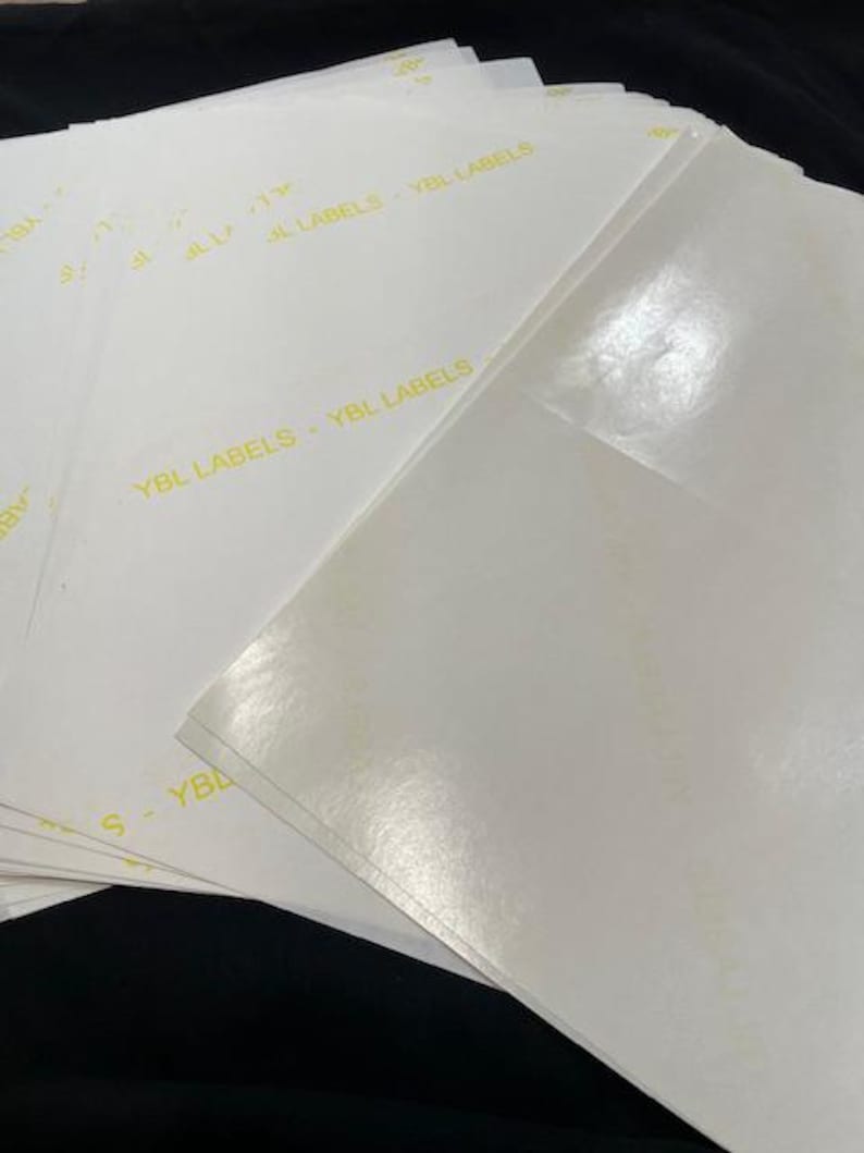 Pode incluir: Uma pilha de etiquetas retangulares brancas e brilhantes com o texto "YBL LABELS" impresso em amarelo.