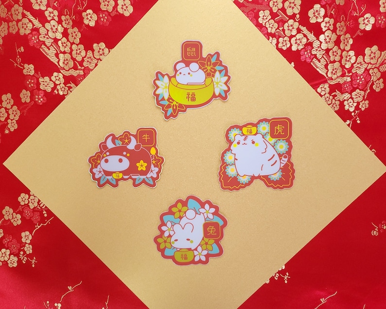 May include: Four colorful stickers featuring Chinese New Year animal illustrations. The stickers feature a red ox, a white cat, a white rabbit in a bowl, and a white rabbit holding a peach. Each sticker has a red background with gold accents and Chinese characters.