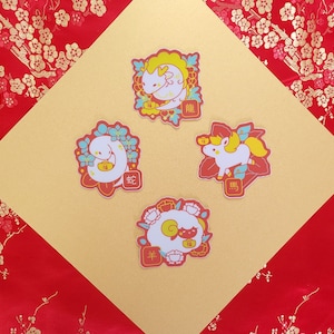 May include: Four colorful stickers featuring Chinese zodiac animals. The stickers are on a gold background with red floral patterns. The animals are a dragon, a snake, a horse, and a sheep. The stickers have Chinese characters on them.