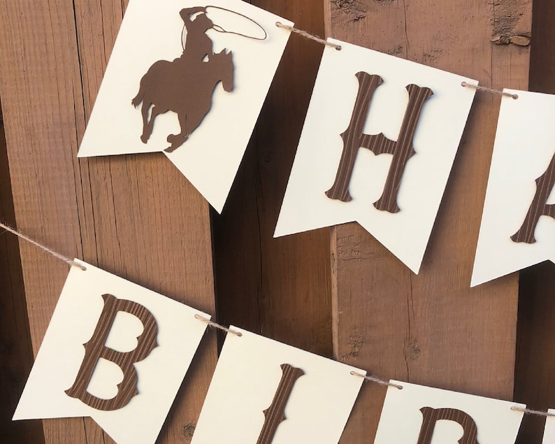 May include: A brown and white banner with the words "Happy Birthday" in brown letters. The banner is decorated with a silhouette of a cowboy riding a horse.